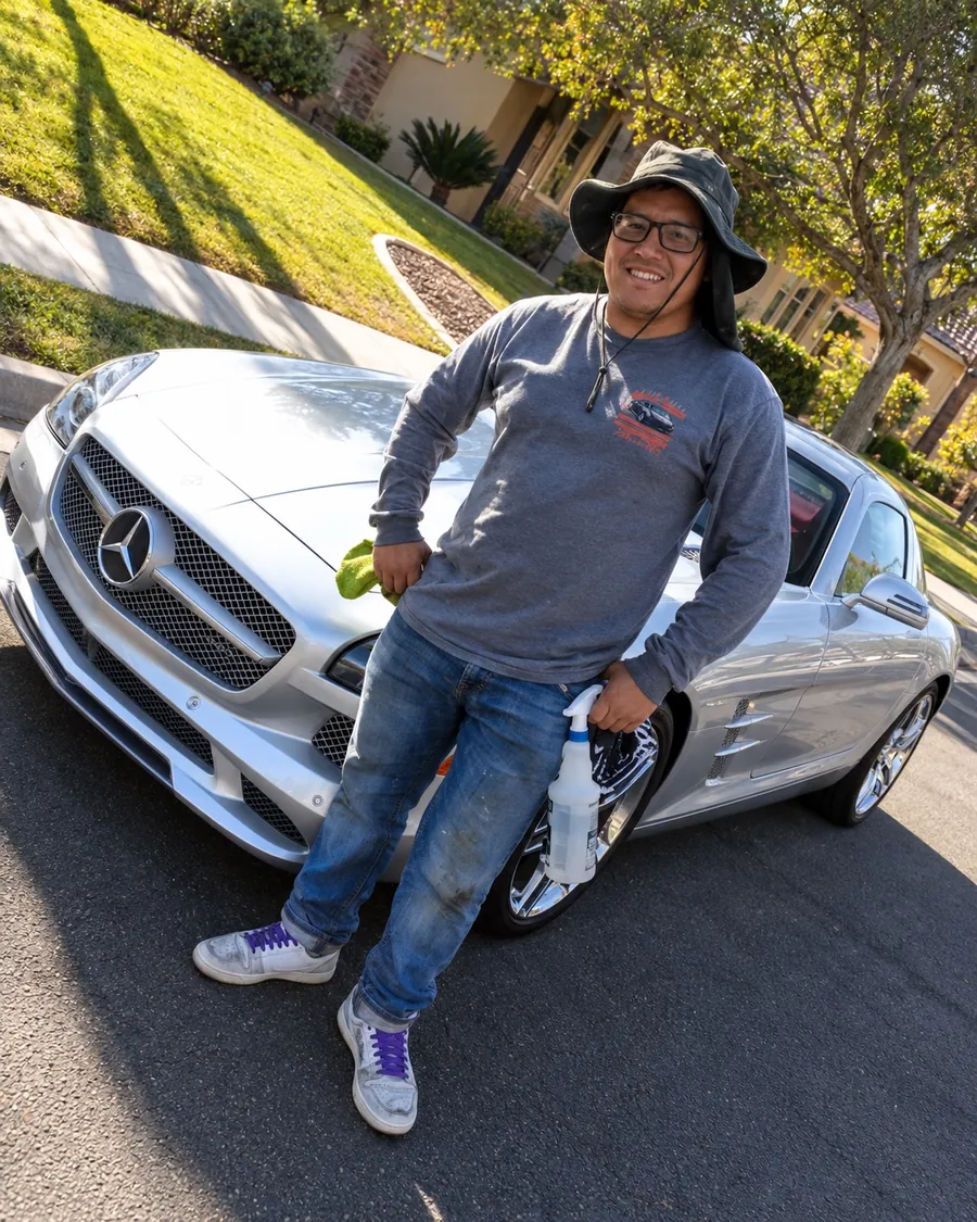 Leo in a bucket hat, leaning on a silver Mercedes with a spray bottle and microfiber towel
