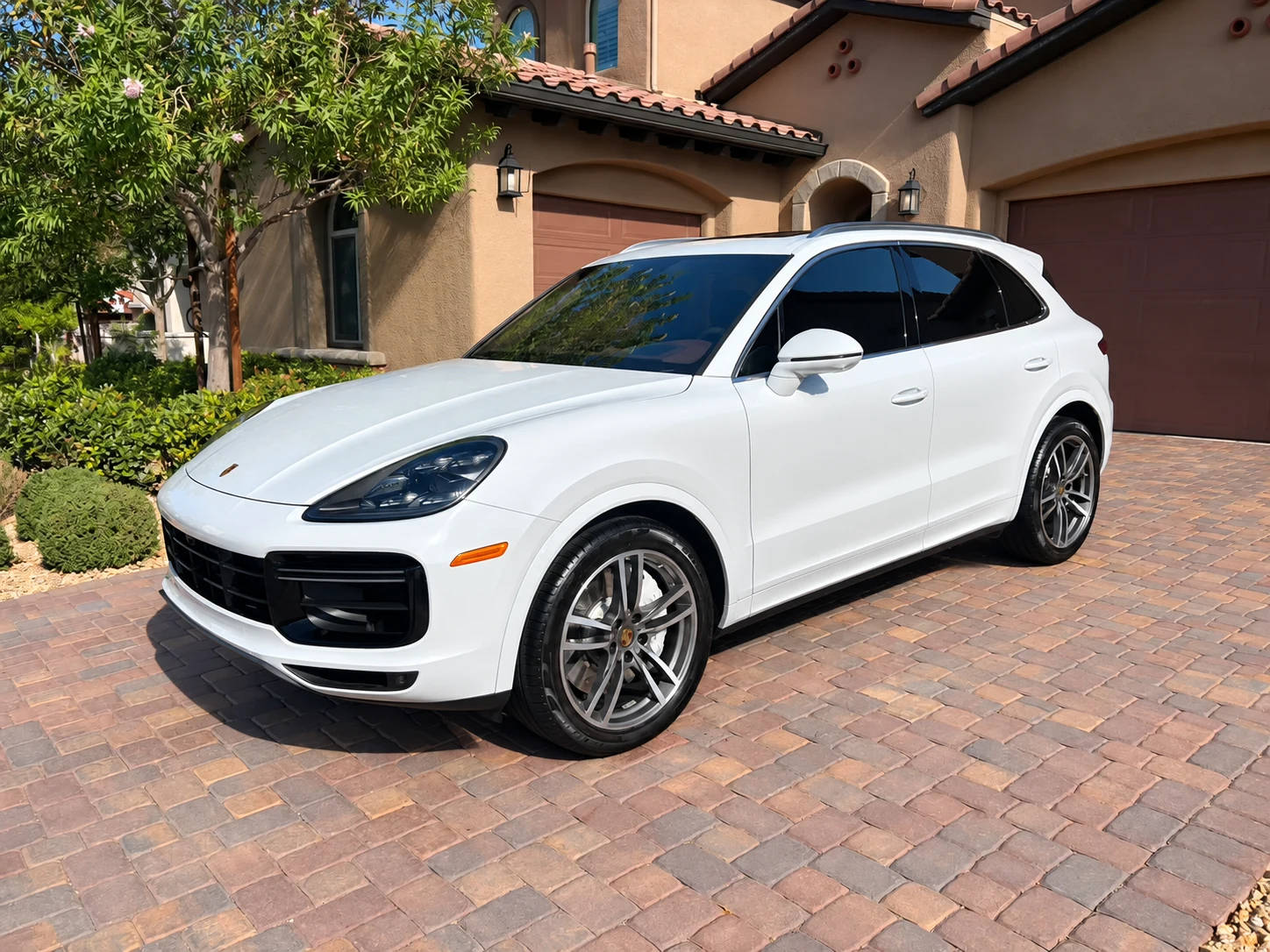 White Porsche Cayenne with silver wheels on a brick driveway